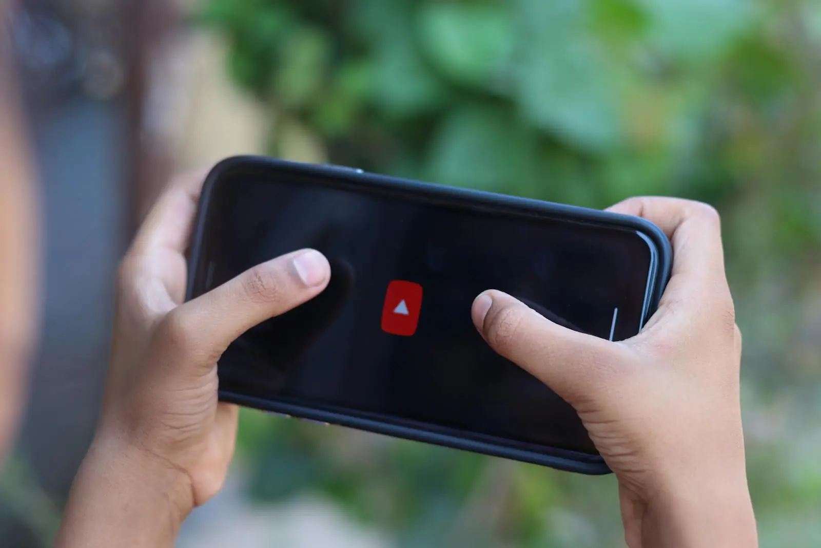 Close-up of hands holding a smartphone displaying a video app icon outdoors.