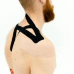Close-up view of kinesio tape applied to a man's shoulder for medical treatment.
